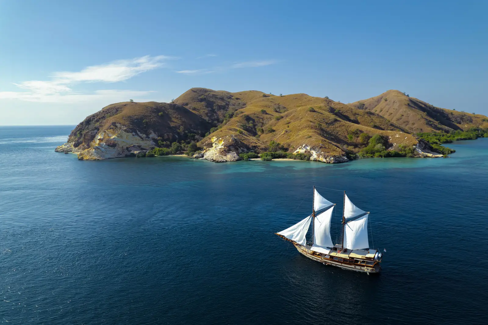 A phinisi under full sail beside the dry hills of Komodo